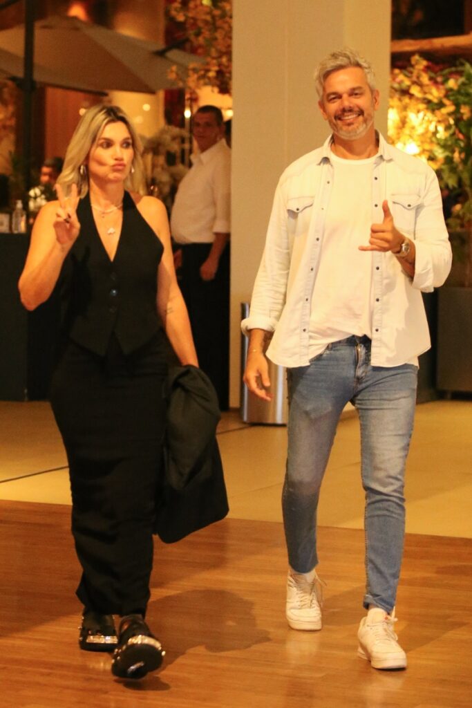 Flavia Alessandra de vestido preto e Otaviano Costa de camisa branca e calça jeans, ambos fazendo sinal de positivo