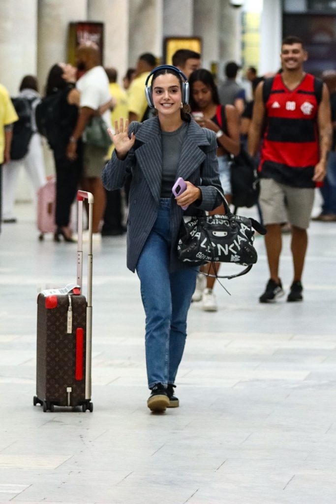 Giovanna Lancellotti de calça jeans, casaco preto, com mala e bolsa no aeroporto