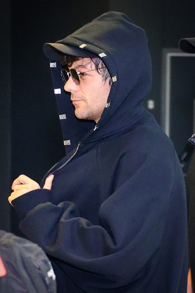 Louis Tomlinson de casaco preto de capuz, óculos escuros 