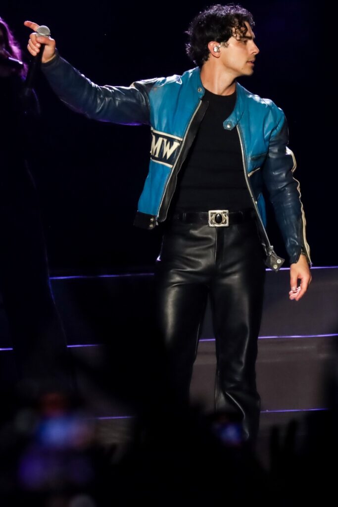 Joe Jonas de calça de couro preta e casaco preto e azul 