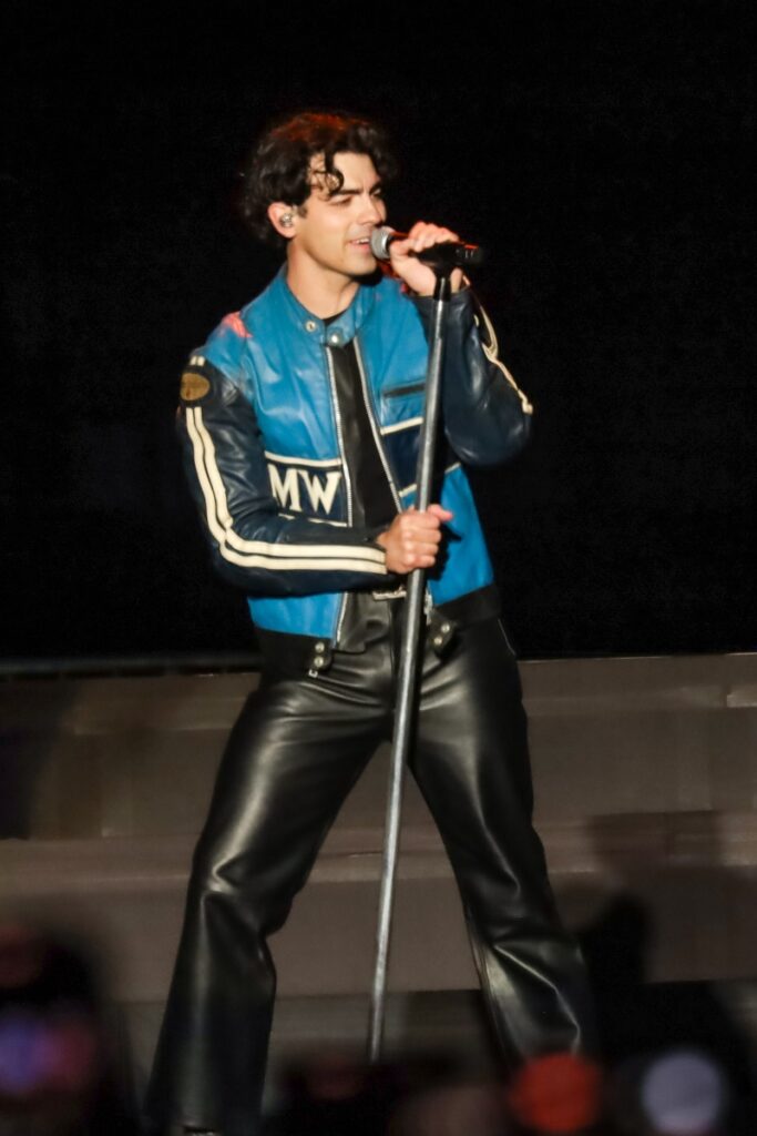 Joe Jonas de calça de couro preta e casaco preto e azul 