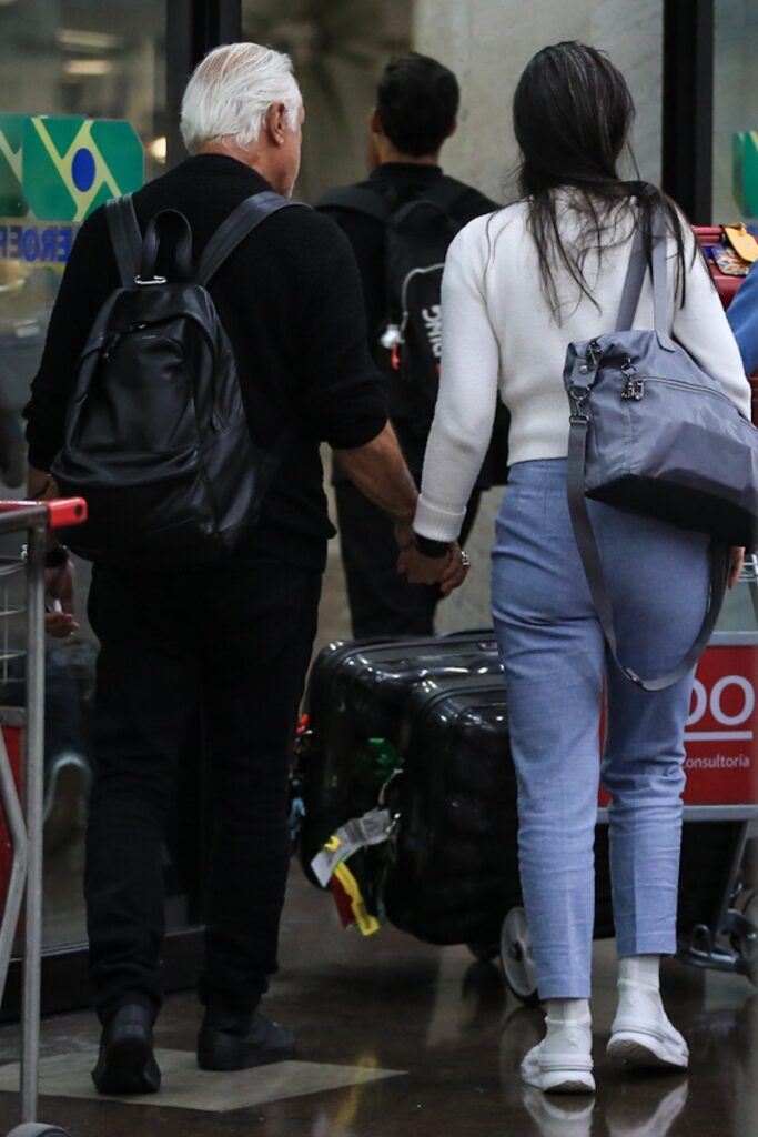 Antônio Fagundes e Alexandra Martins de mãos dadas, de costas, no aeroporto 