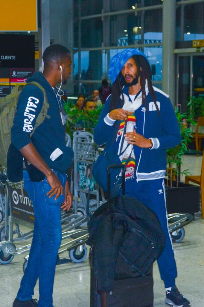 Julian Marley de casaco e calça azul, boina azul, no aeroporto  no aeroporto