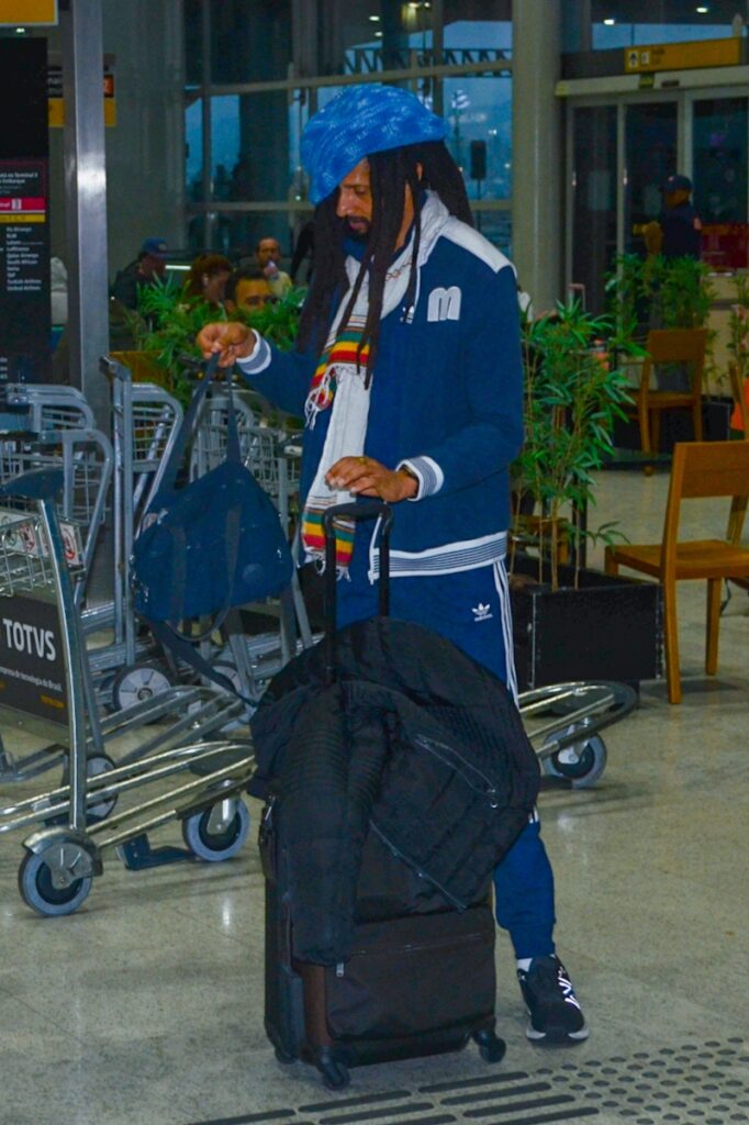 Julian Marley de casaco e calça azul, boina azul, no aeroporto  no aeroporto
