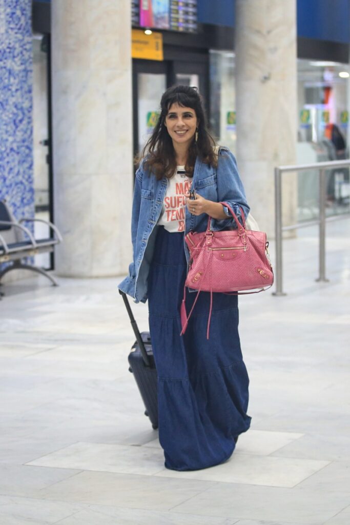 Maria Ribeiro de bolsa rosa e jeans, no aeroporto