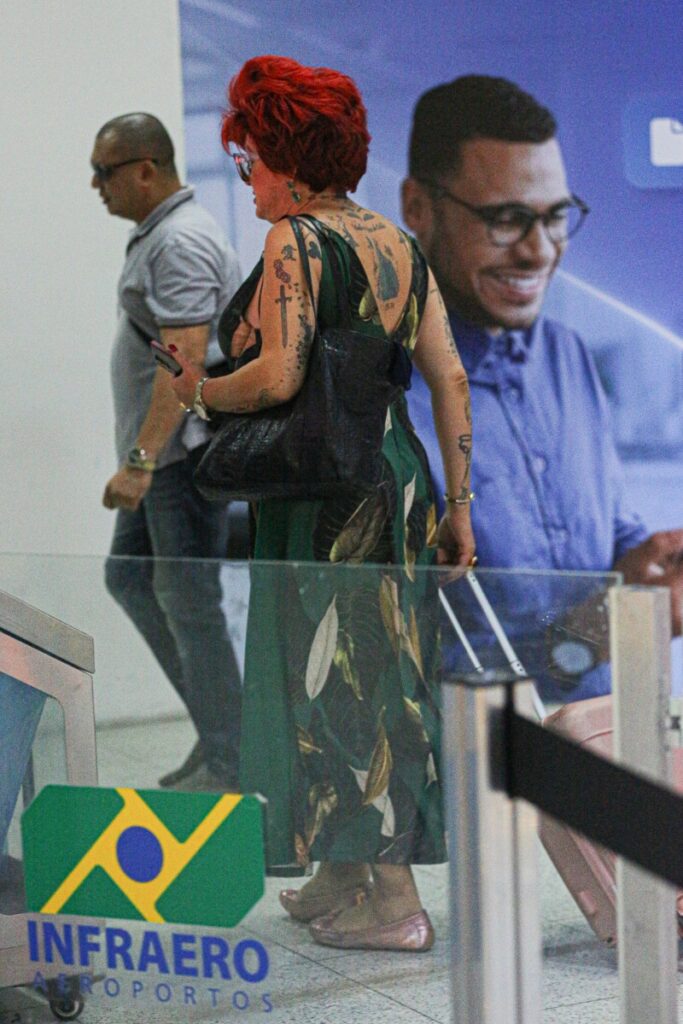 Nany People de vestido estampado verde, no aeroporto, com mala 