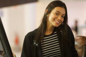 Alane sorrindo, de jaqueta preta e camisa de listras preto e branco