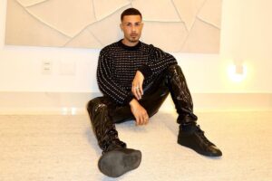 Carlinhos Maia todo de preto, sentado no chão