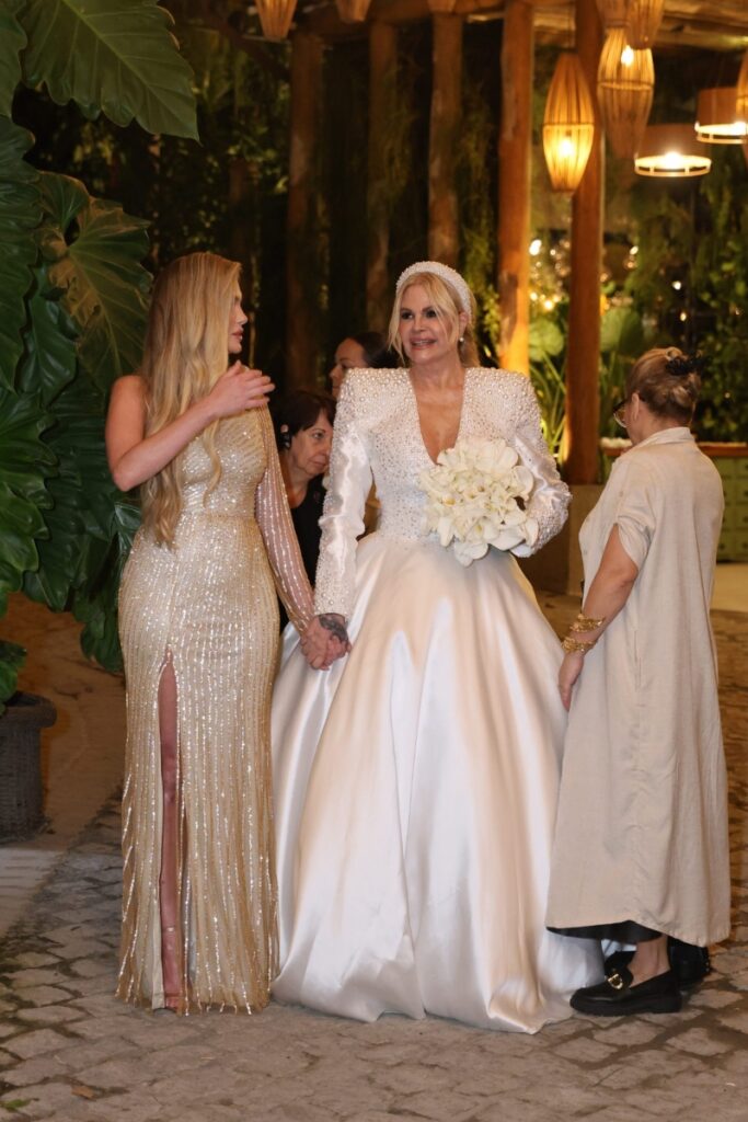 Casamento Monique Evans - Bárbara Evans de vestido longo dourado com fenda, de mãos dadas com a mãe, vestida de noiva 