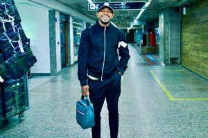 Davi de moletom preto e boné, no aeroporto