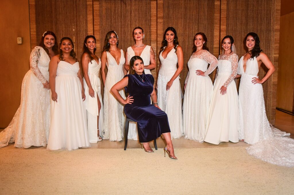 Estilista Flayza Vieira de vestido azul escuro cercada por noivas 