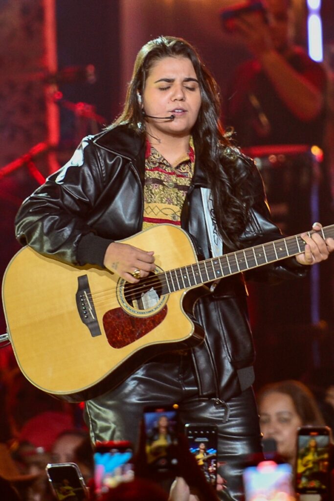 Yasmin Santos tocando violão, de jaqueta de couro preta 