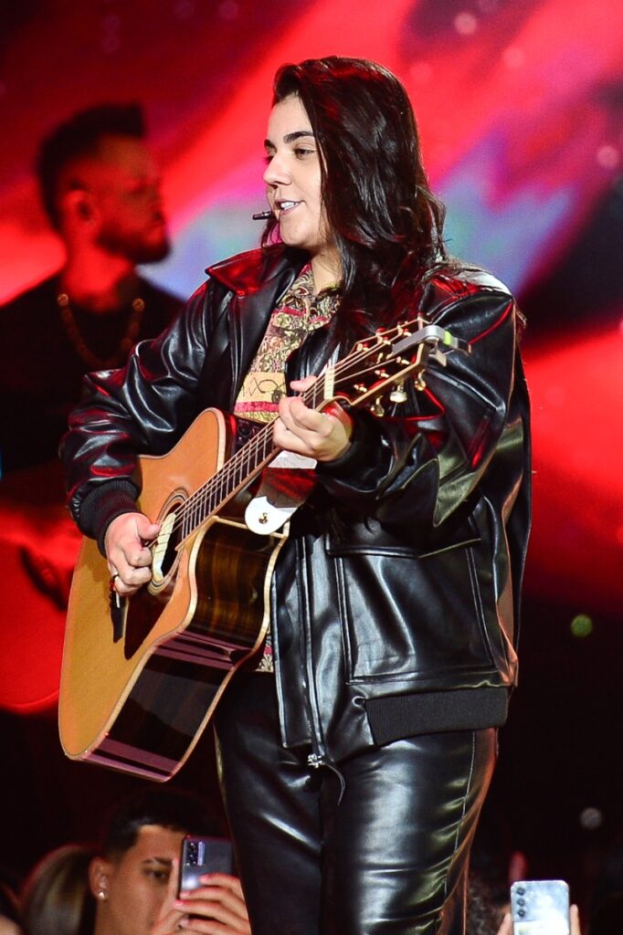 Yasmin Santos tocando violão, de jaqueta de couro preta 