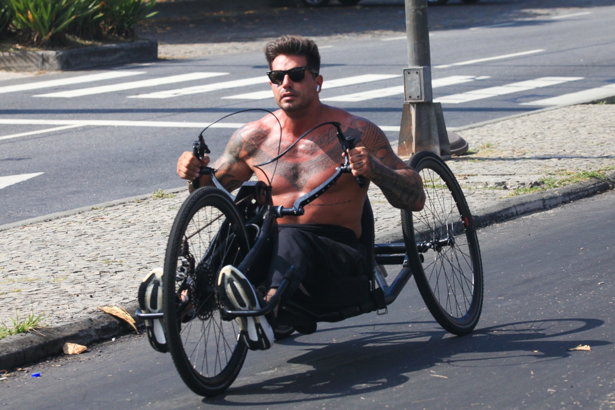 Fernando Fernandes andando de bicicleta adaptada, sem camisa e de óculos escuros