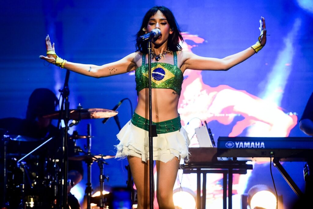 Danna Paola de saia branca e cropped com estampa da bandeira do Brasil, cantando