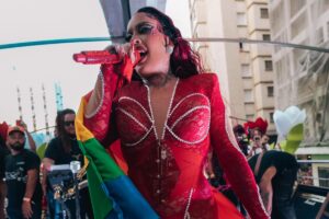 gloria groove com look vermelho e bandeira lgbt cantando na parada do orgulho