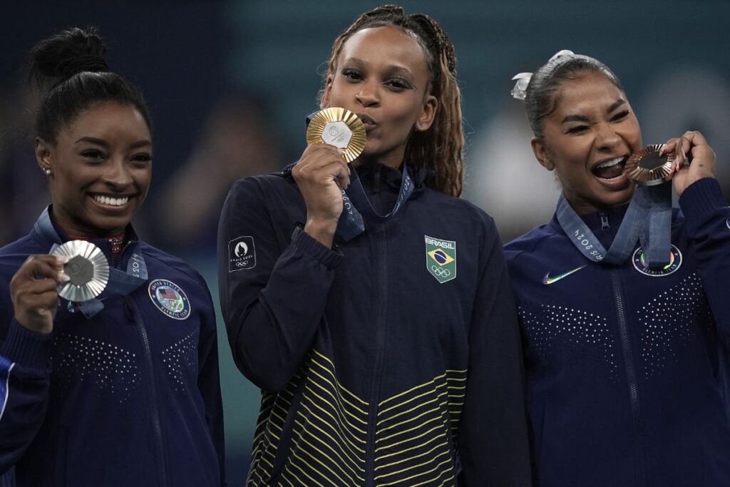 Rebeca Andrade no alto do pódio ao lado de Simone Biles e Jordan Chiles 