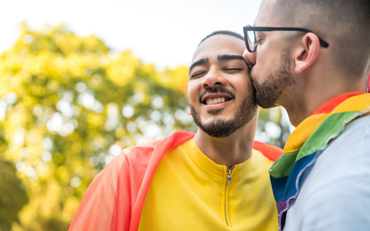 Casal LGBTQIA+ se beijando com a bandeira