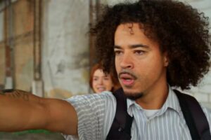 Ryan (L7NNON) com arma protegendo Kami (Giovanna Lancellotti) em Dona de Mim